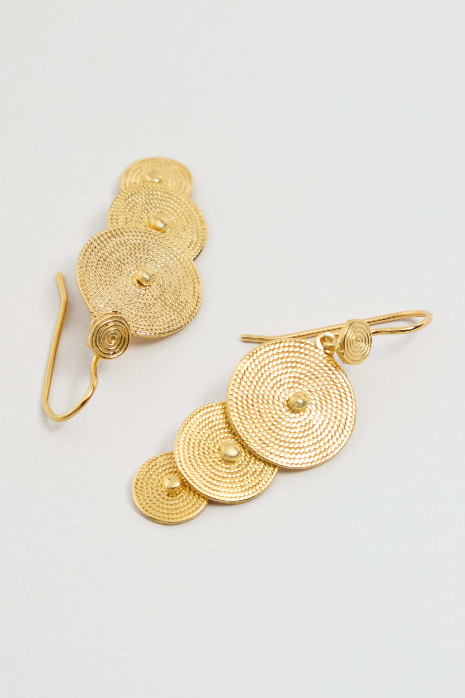 The Gold Vermeil Orbit Disc Earrings feature three textured circular discs and a hook fastening, shown on a light background.