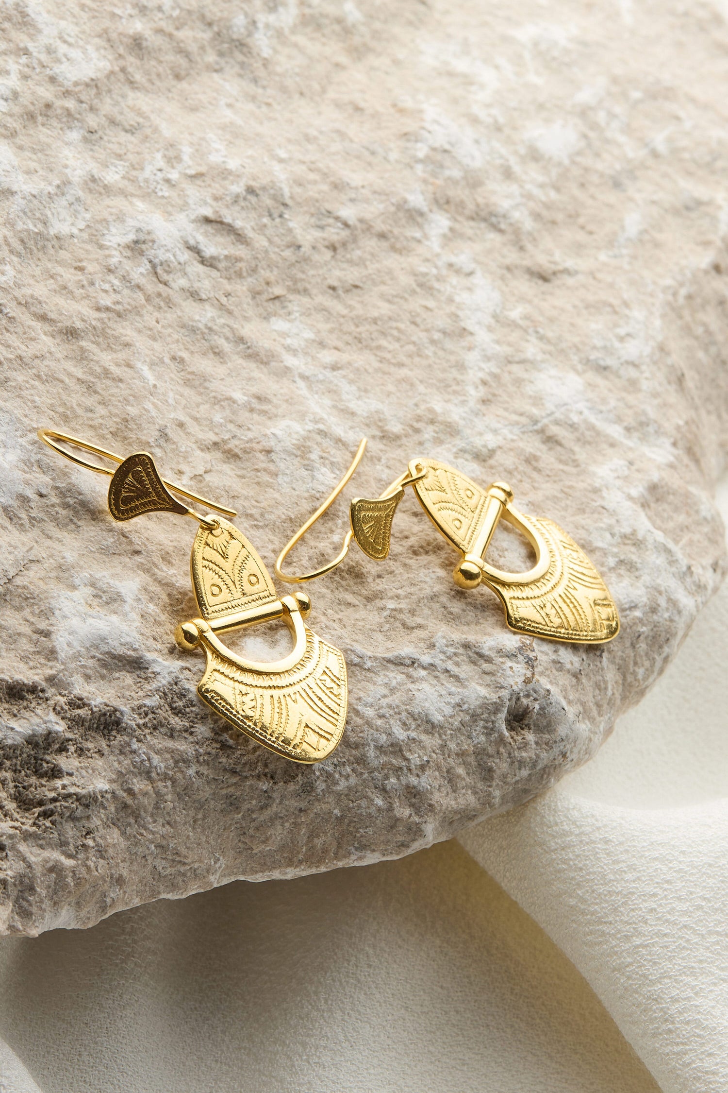 A pair of Engraved Gold Vermeil Tuareg Earrings on a rock.