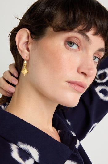 A woman with short dark hair wears a blue patterned top and the Gold Vermeil Faceted Drop Earrings, tilting her head and touching her neck as she looks at the camera.