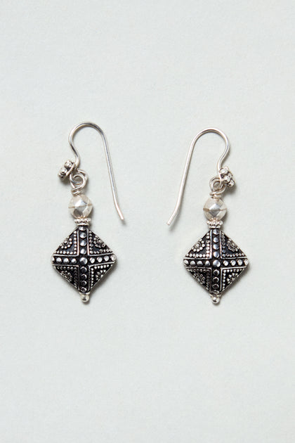 The Silver Faceted Drop Earrings feature sterling silver diamond-shaped pendants with small faceted beads above each, displayed on a light gray background.