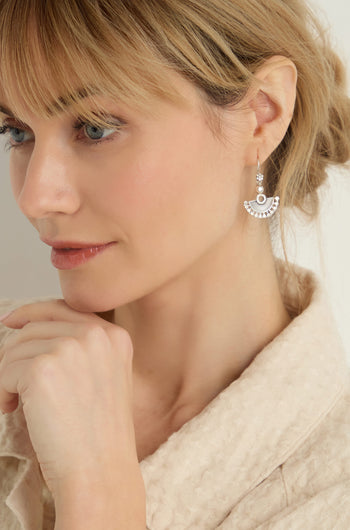 Woman with blonde hair wearing a beige textured top and Silver Mini Fan Earrings, resting her chin on her hand and looking to the side.