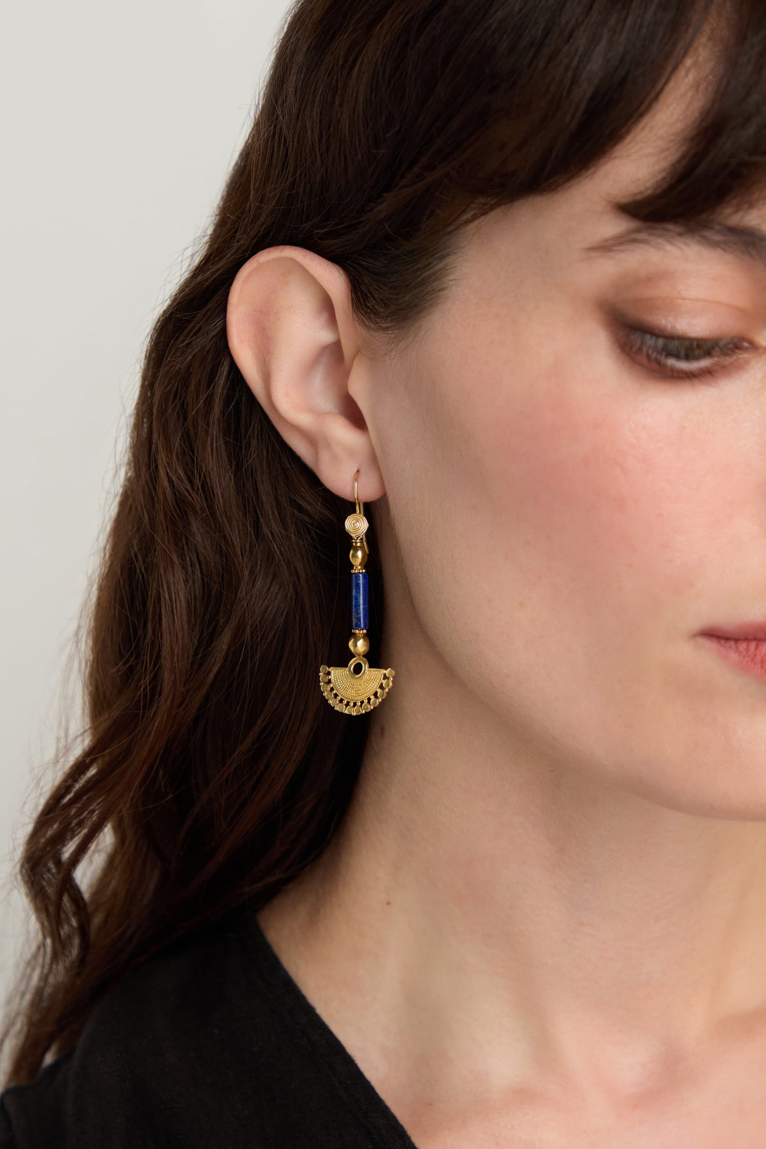 Close-up of a woman wearing Gold Vermeil Lapis Fan Earrings shaped like a half-circle, with her brown hair down and part of her face visible.