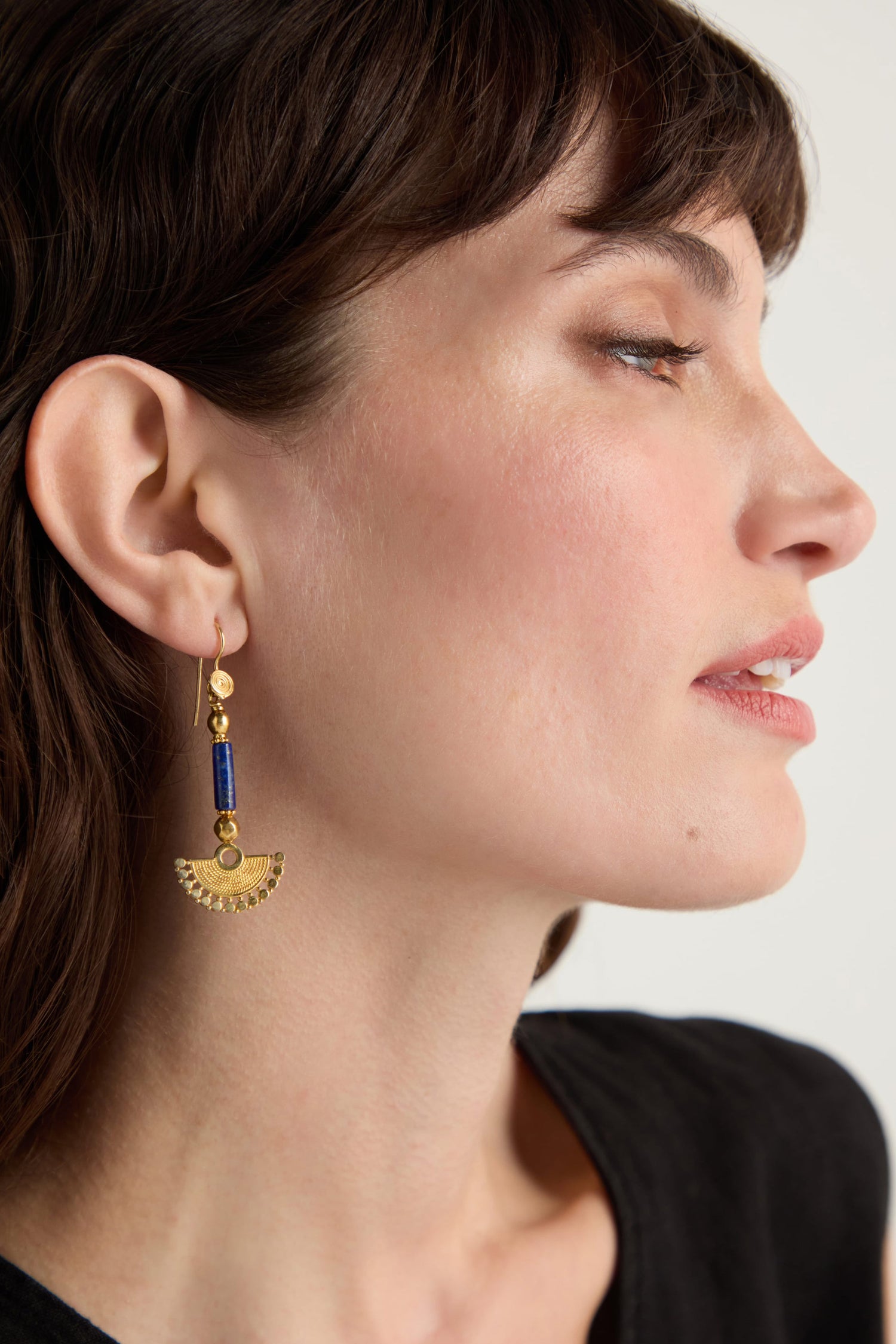 A woman with short brown hair wears Gold Vermeil Lapis Fan Earrings with blue and gold bead details, shown in a close-up side profile.