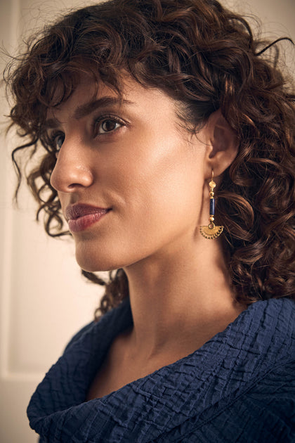 A person wearing Gold Vermeil Lapis Fan Earrings, which feature a blue rectangular stone and a semicircular fan-shaped pendant.