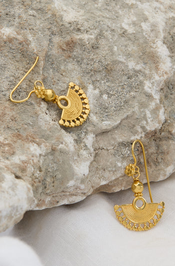 Two intricately designed 18ct Gold Vermeil Mini Fan Earrings are placed on a rough stone surface. One earring dangles from the stone, while the other lies flat beside it, exuding bohemian elegance.