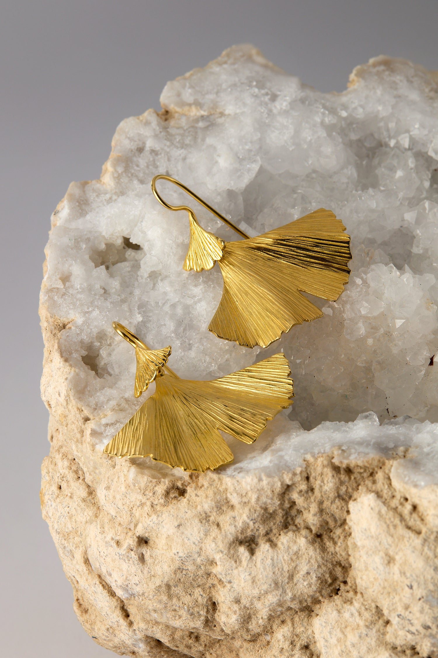 Gold Vermeil Ginkgo Leaf Earrings grace a white textured stone, epitomizing nature-inspired elegance with their exquisite design.