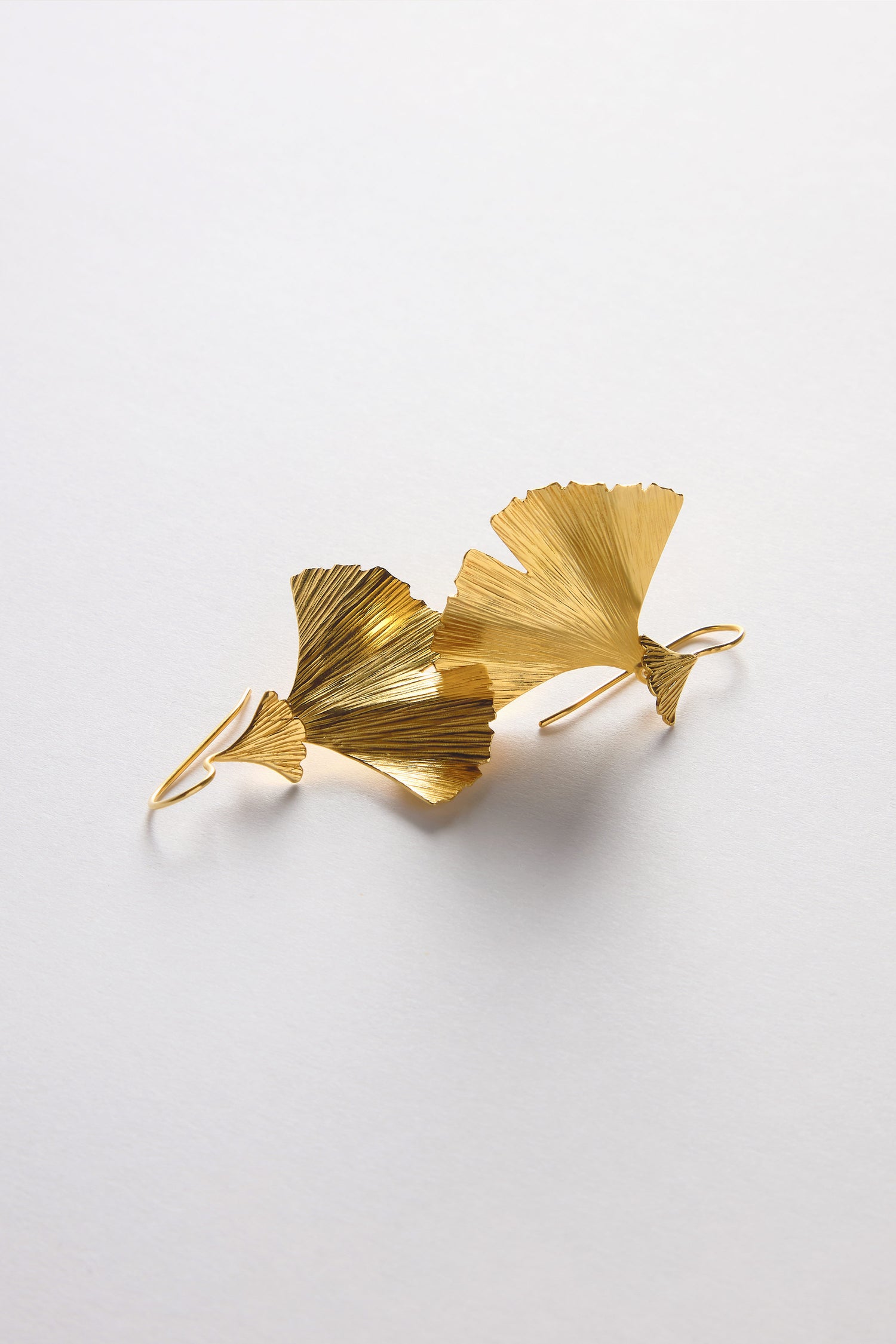 The Gold Vermeil Ginkgo Leaf Earrings elegantly mimic nature, featuring gold leaf-shaped designs on a white background. Ideal for nature-lovers, their stunning gold vermeil finish enhances their elegance.