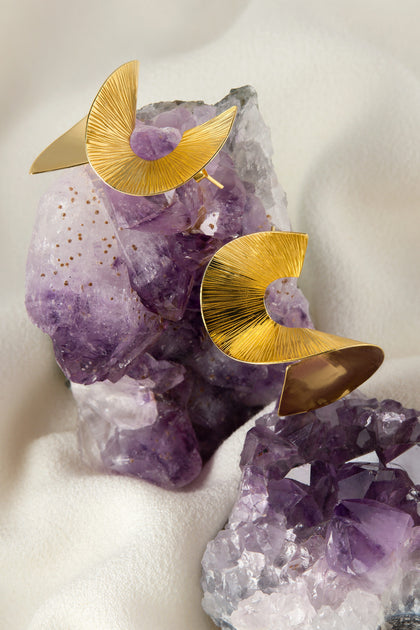 The Gold Vermeil Twist Earrings sit elegantly on purple amethyst crystals against a white fabric background, showcasing their sophisticated 18k gold vermeil finish.