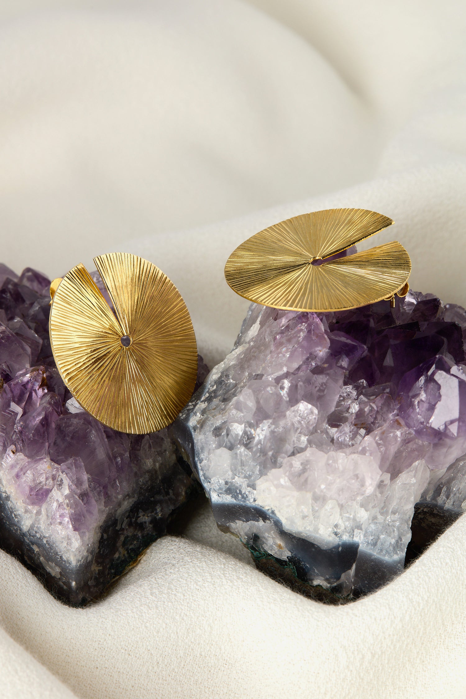 The Large Gold Vermeil Lotus Leaf Earrings, featuring an organic textured design, rest elegantly on purple amethyst crystals against a beige fabric background.