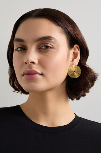 A person with short brown hair, wearing a black shirt and Large Gold Vermeil Lotus Leaf Earrings, looks directly at the camera.