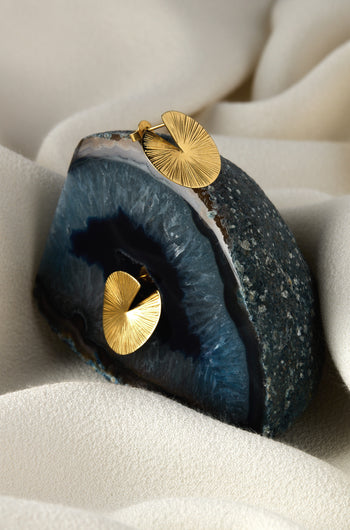 Small Gold Vermeil Lotus Leaf Earrings elegantly rest on a blue geode, highlighting their sculptural design against a textured beige fabric. The geode's natural veins contrast beautifully with the earrings' graceful silhouette.