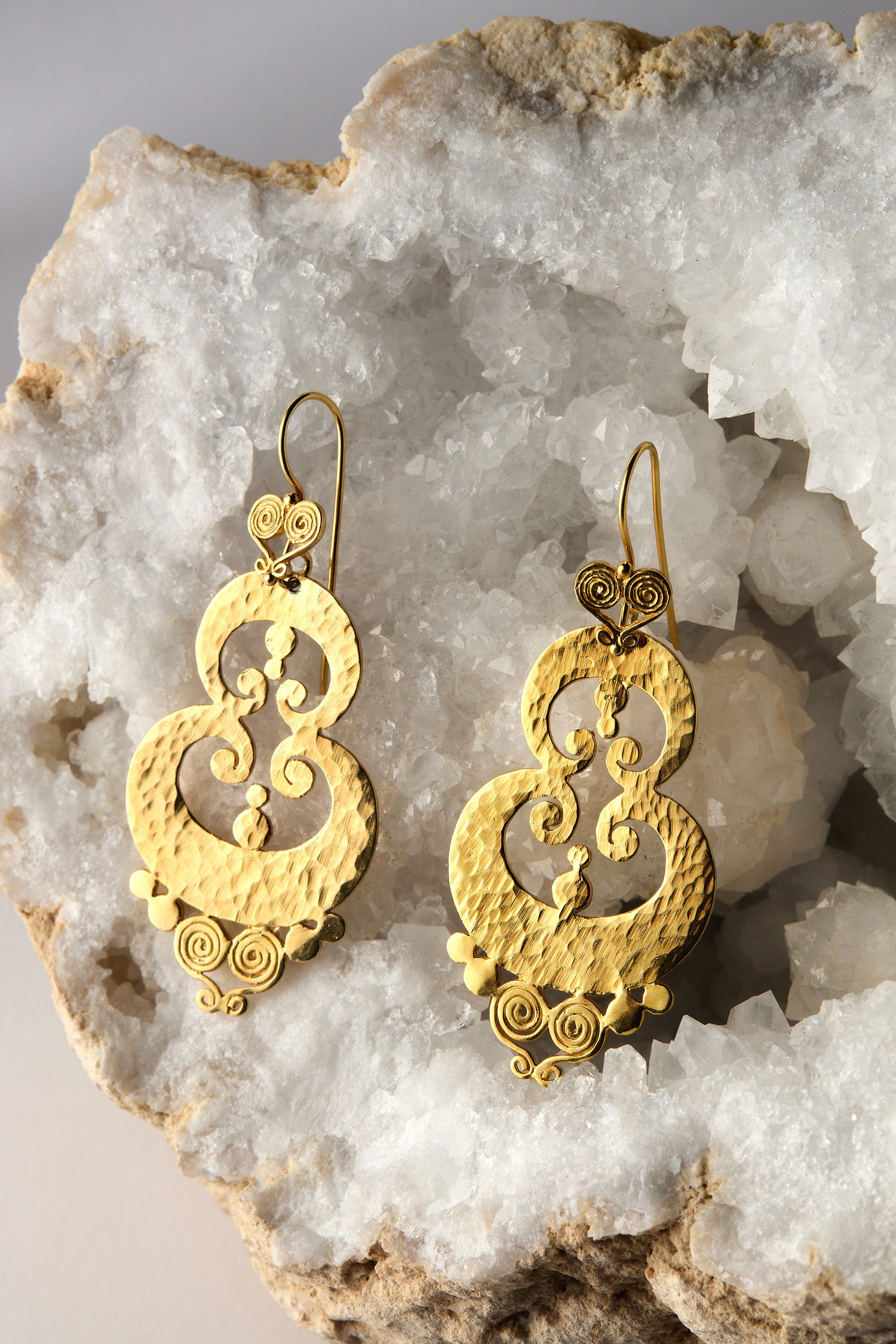 The Gold Vermeil Sumba Earrings feature a circular textured design with intricate filigree, displayed on crystalline rock.