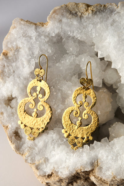 The Gold Vermeil Sumba Earrings feature a circular textured design with intricate filigree, displayed on crystalline rock.