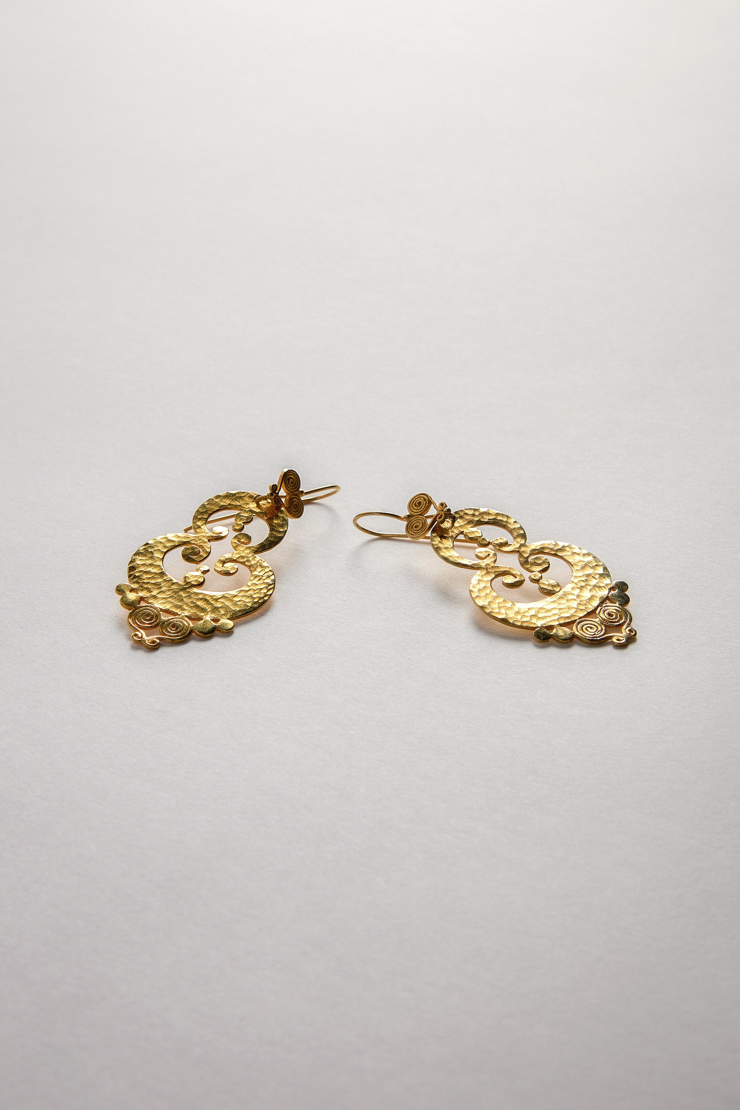 Two Gold Vermeil Sumba Earrings featuring circular and floral designs rest on a white surface, highlighting their artisanal appeal with intricate filigree detailing.