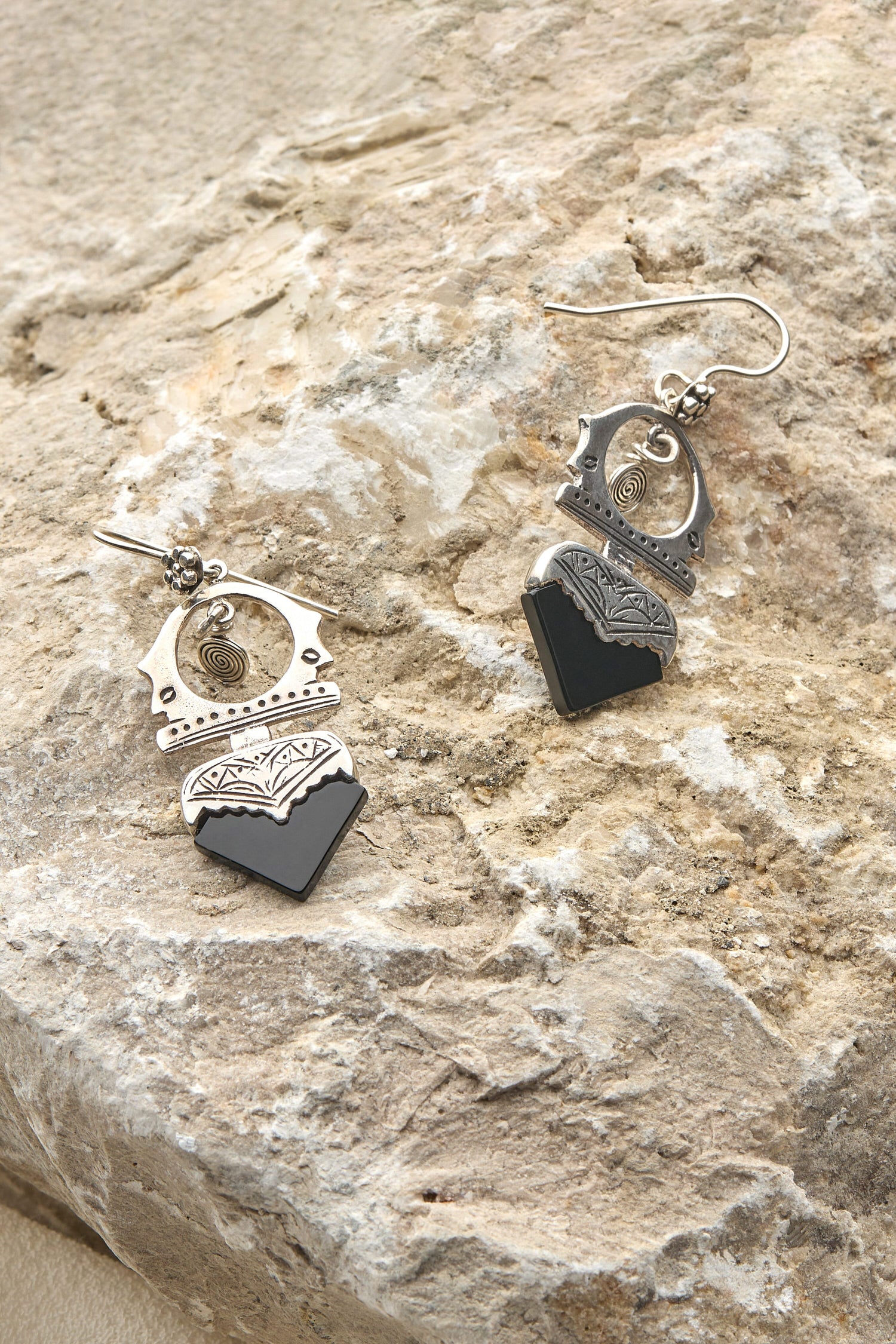 A pair of Silver and Black Onyx Tuareg Earrings resting on a rock.