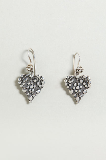 Add a delicate touch to any look with the Silver Heart Earrings—sterling silver drop earrings featuring heart shapes with floral and dot details, perfect against a light background.