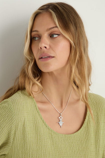 A woman with wavy blonde hair, in a light green textured top and a Silver Tuareg Pendant necklace, looks to the side against a plain background.