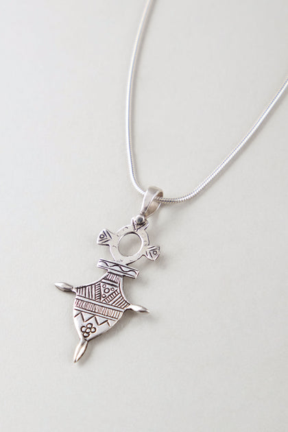 The Silver Tuareg Pendant is a sterling silver necklace featuring an abstract geometric human figure with engraved patterns, making it a striking piece of geometric jewelry shown against a light background.