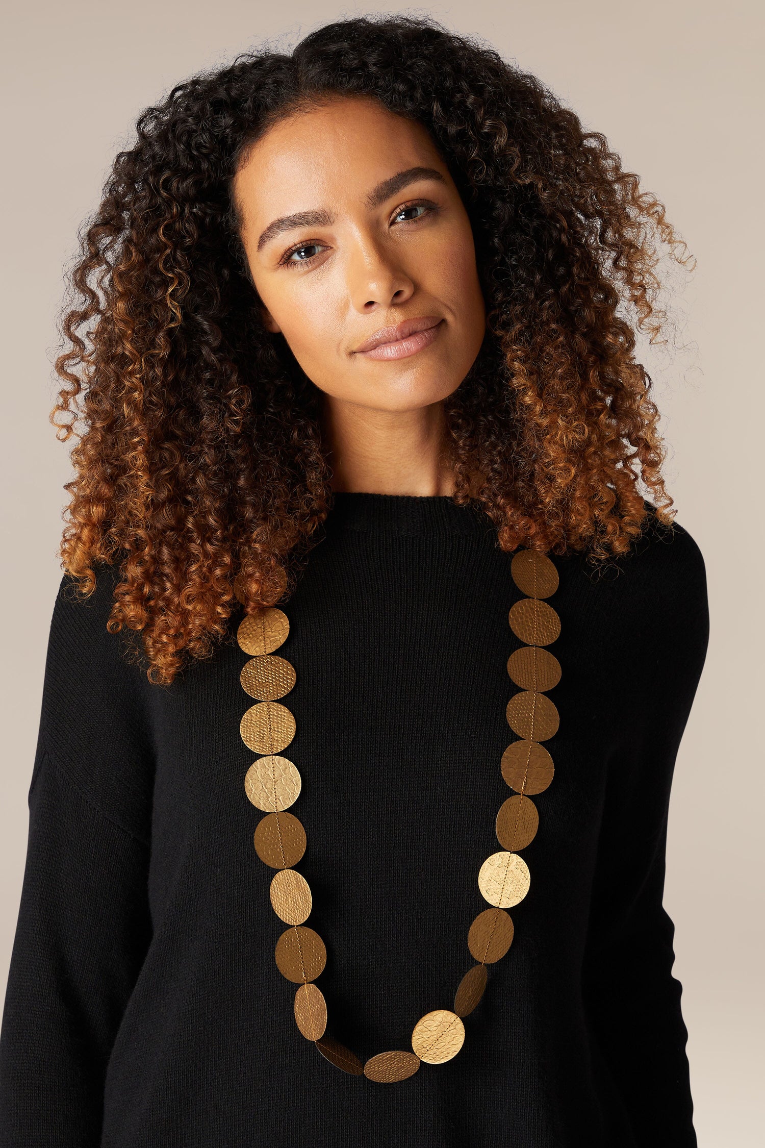 A woman wearing a black sweater with a gold necklace, featuring the Dotty Necklace.
