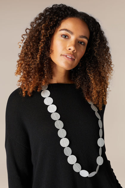A woman wearing a black sweater and a silver necklace adorned with paper beads, also known as the Dotty Necklace.