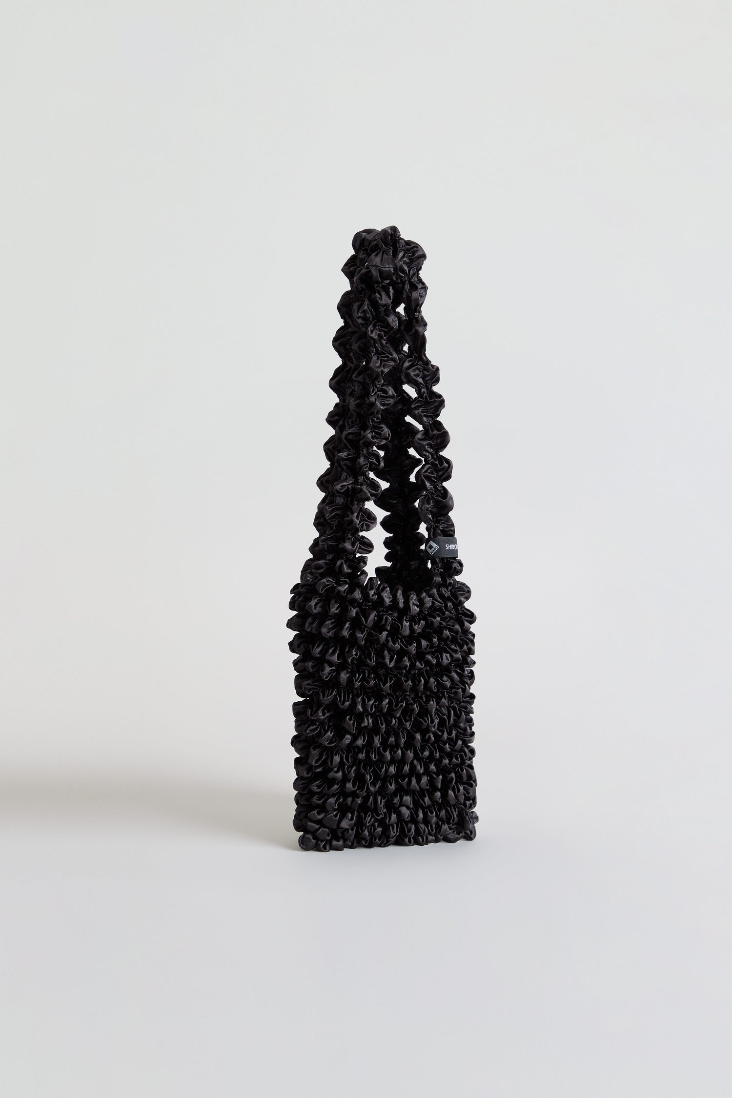 Black Shibori Pleated bag with a textured, elongated body and matching top handle.
