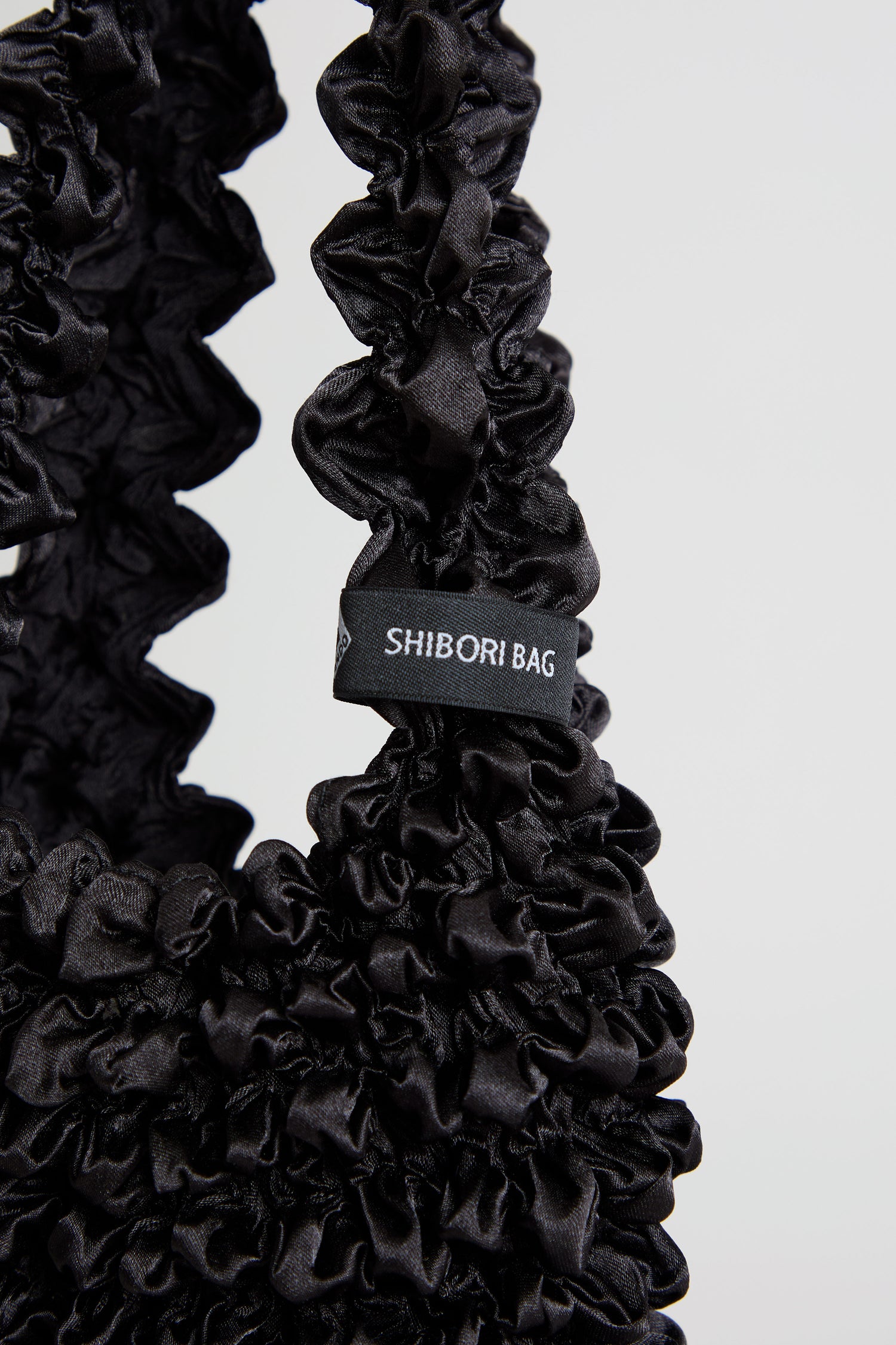 Black Shibori Pleated Bag with a gathered strap and a tag that reads “SHIBORI BAG.”