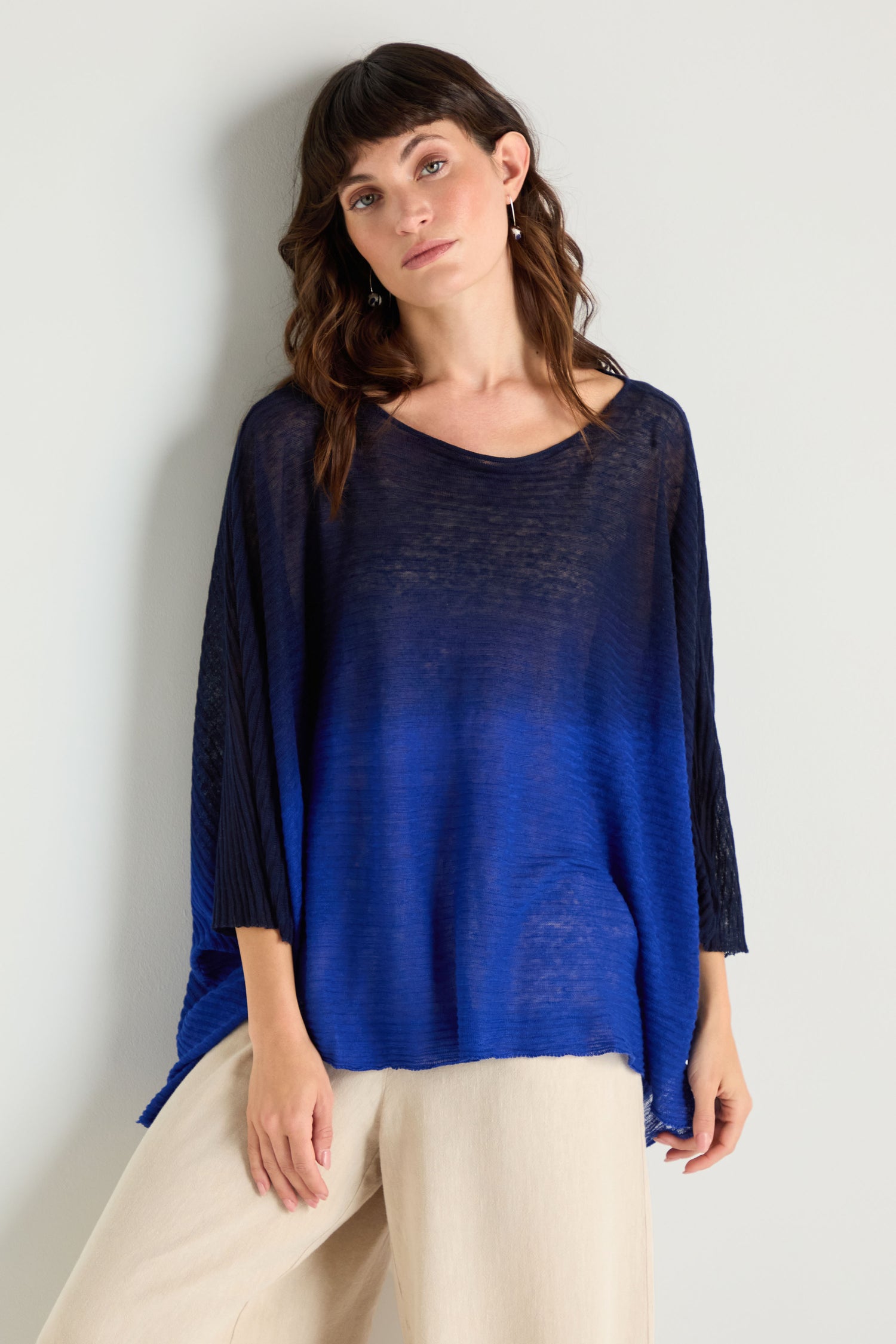 A woman stands against a light wall wearing the Navy Blue Dip Dye Knit Easy Top with three-quarter sleeves, paired with light beige pants.