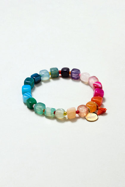 The Artisanal Rainbow Agate Bead Bracelet features multicolored irregular agate stones, a small orange tassel, and a round gold charm—handmade in Scotland and displayed against a light background.