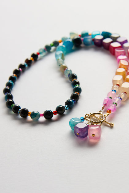 The Artisanal Rainbow Agate Toggle Necklace is displayed on a white surface, showcasing colorful round and faceted blue, pink, and multicolor agate beads with an elegant sterling silver toggle clasp.