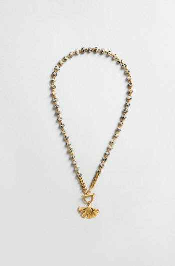 The Dalmatian Stone Ginkgo Leaf Necklace features gold and silver beads, a textured ginkgo leaf pendant, and a toggle clasp, displayed on a flat neutral background.