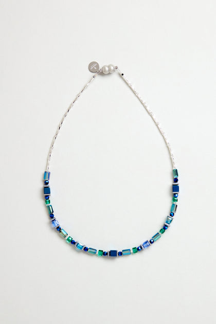 The Blue Hematite Necklace features blue and green square and rectangular beads, faceted glass crystals on a thin white string, handmade in Scotland with a small silver charm and clasp.