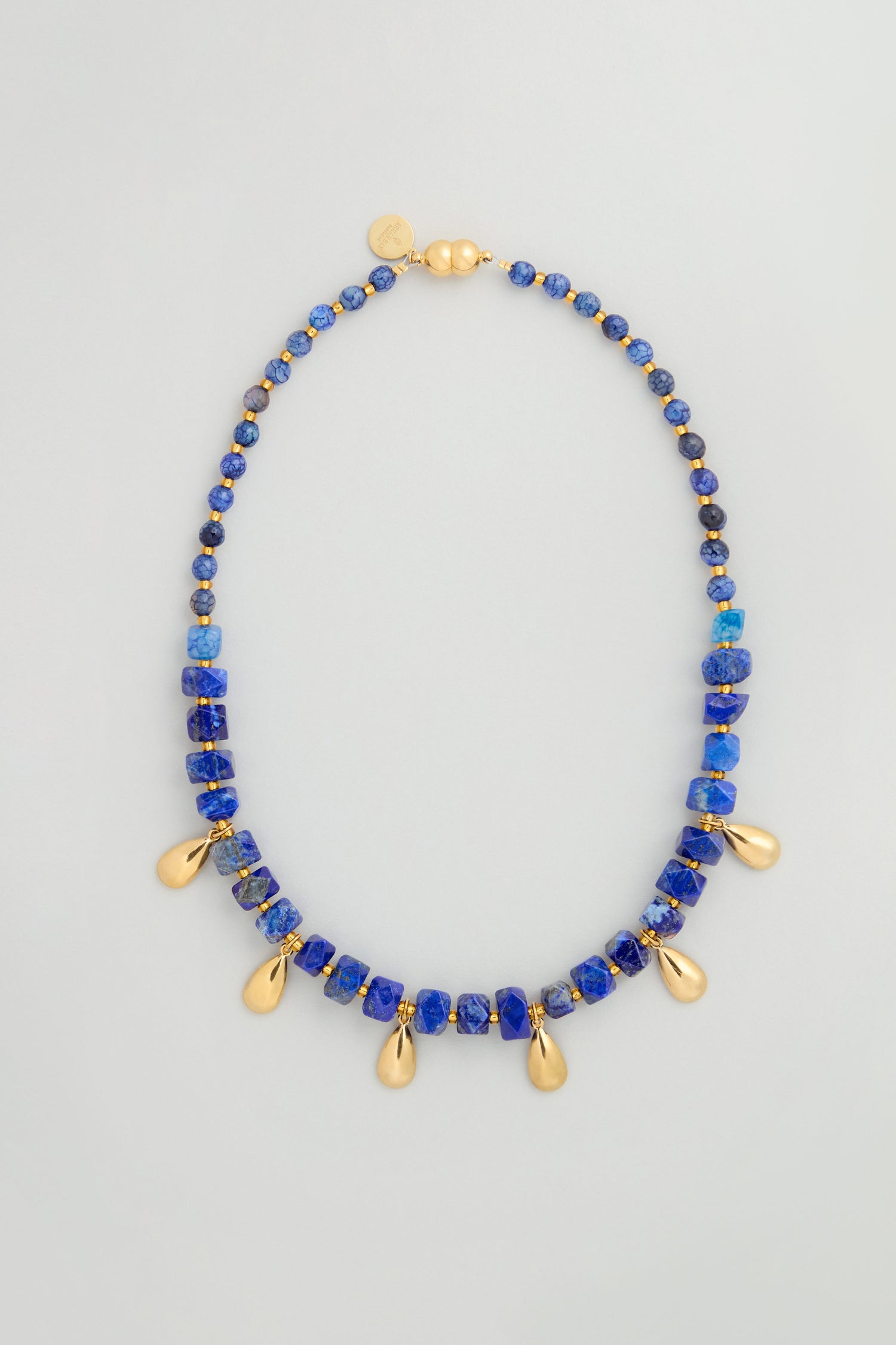The Lapis Lazuli Teardrop Necklace is handmade in Scotland, featuring blue lapis lazuli stones and gold teardrop pendants, finished with a gold clasp and a small gold tag.