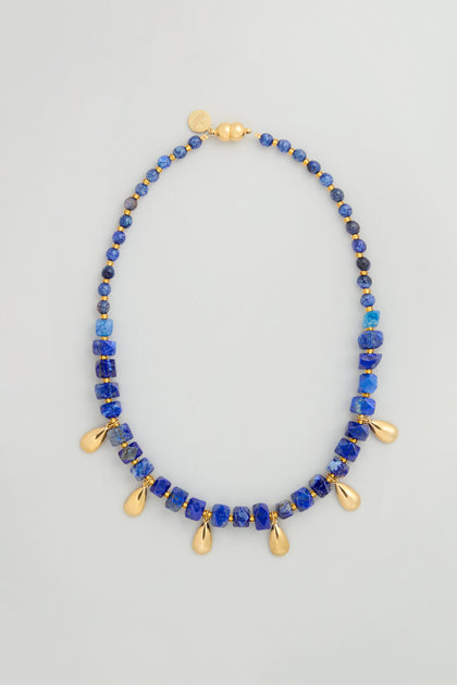 The Lapis Lazuli Teardrop Necklace is handmade in Scotland, featuring blue lapis lazuli stones and gold teardrop pendants, finished with a gold clasp and a small gold tag.