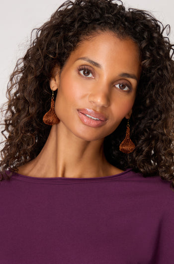 A woman with curly hair in a purple top models Hand Crocheted Teardrop Earrings, highlighting their artisanal craftsmanship against a plain background.