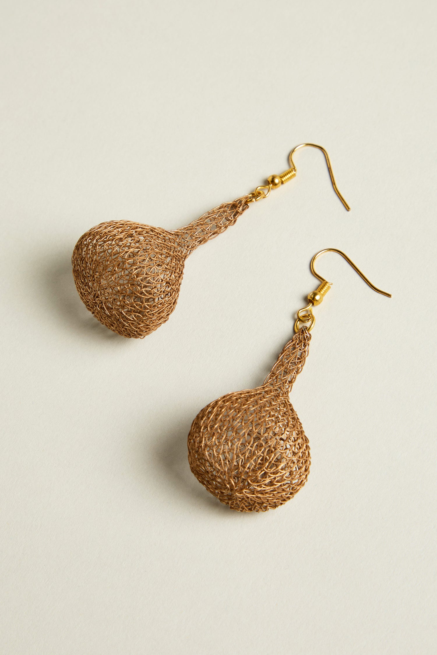 The Hand Crocheted Teardrop Earrings are gold-colored with hook closures, intricately woven with metallic threads to showcase artisanal craftsmanship on a light background.