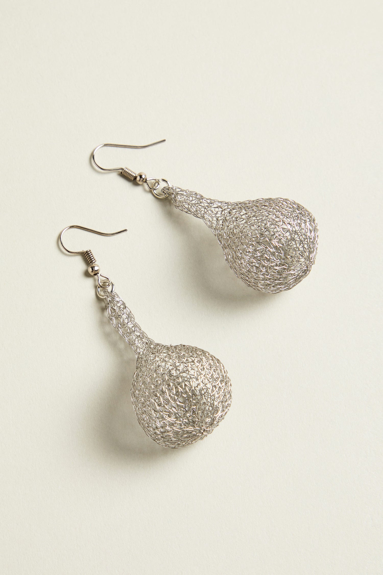 The hand crocheted craftsmanship is evident in these teardrop earrings, where intricate metallic threads form a delicate pattern on the light surface.