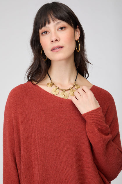 Woman with straight dark hair wears a rust-colored Two Pocket Oversize Knit, gold hoop earrings, and a gold statement necklace while looking at the camera against a plain background.
