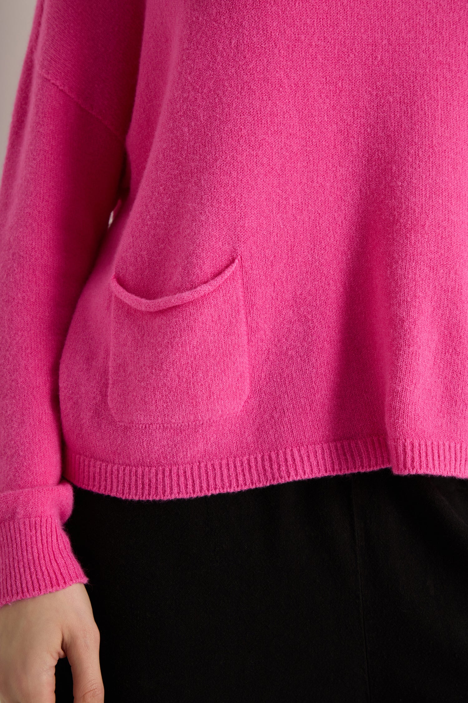 A person wearing a bright pink women's Two Pocket Knit sweater, perfect for everyday layering, paired with black pants.