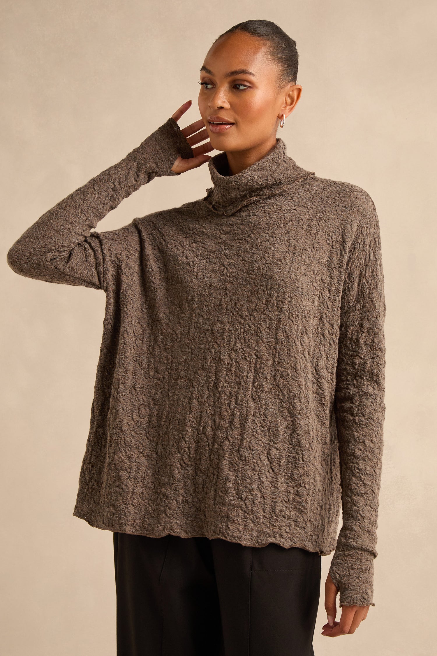 A person wearing the Taupe Textured Merino Roll Neck Top with long sleeves and black pants, standing against a neutral background.
