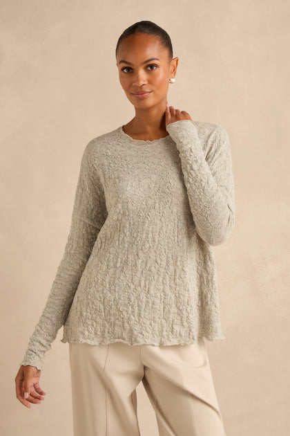 Woman wearing a Silver Textured Merino Scoop Neck Top and beige pants, standing against a plain beige background.