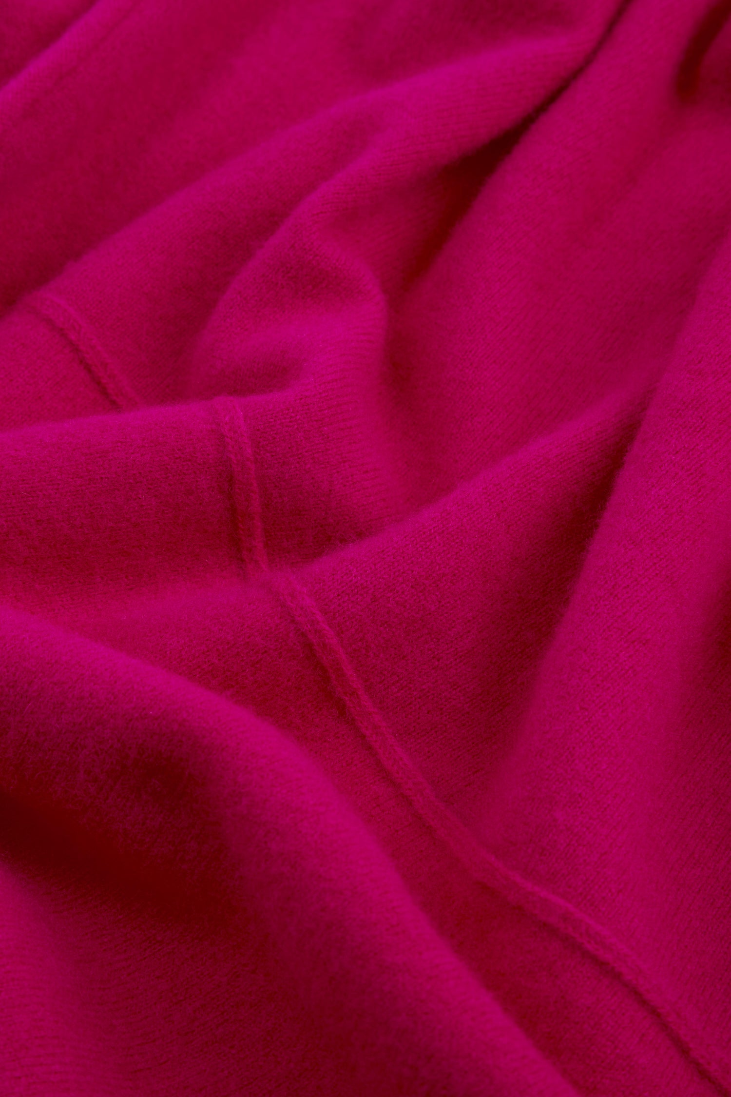 Close-up of magenta merino wool fabric with visible seams and gentle folds, reminiscent of the cosy texture of the Magenta Merino Wool Cowl Neck Jumper.