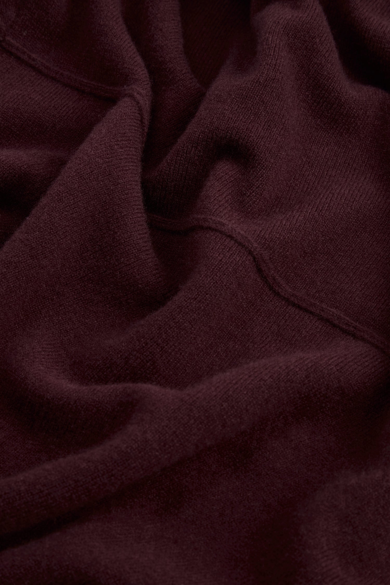 Close-up of the Plum Merino Wool Cowl Neck Jumper, showcasing its soft, dark plum knit with visible texture and seams, gently wrinkled and folded for a cosy look.