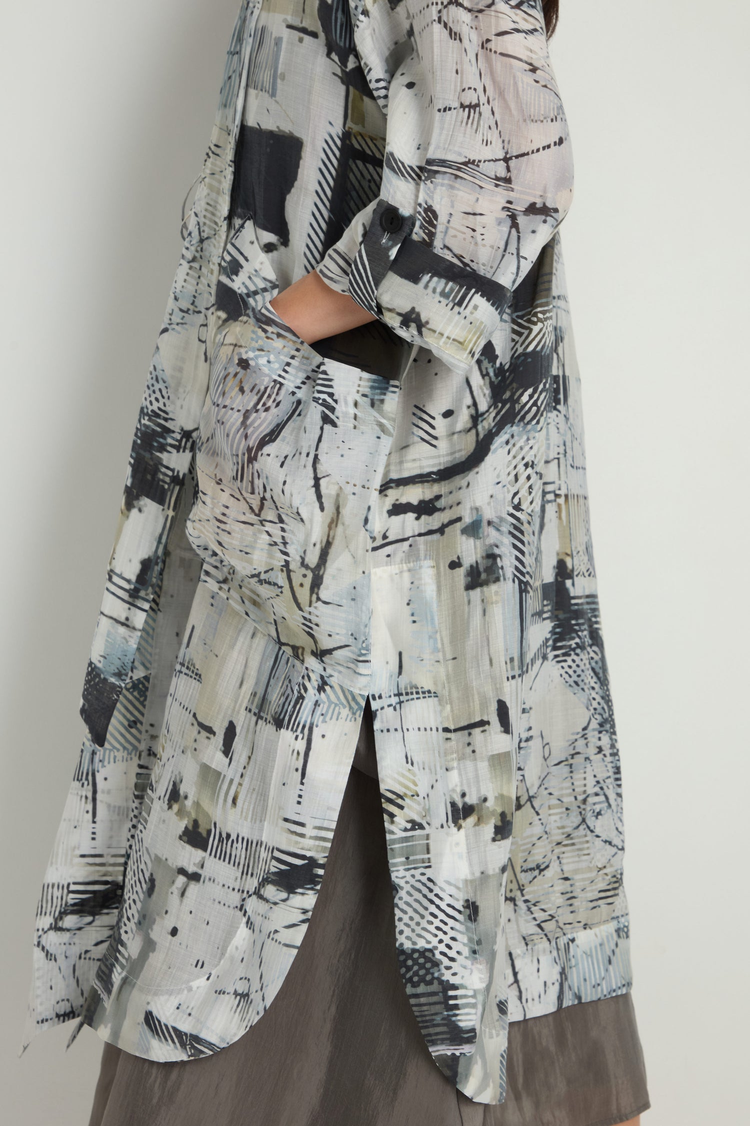 A person wears the Shaded Print Long Coat, a long sheer Tencel blend button-up with an abstract shaded pattern and rolled sleeves, layered over a dark skirt against a plain background.
