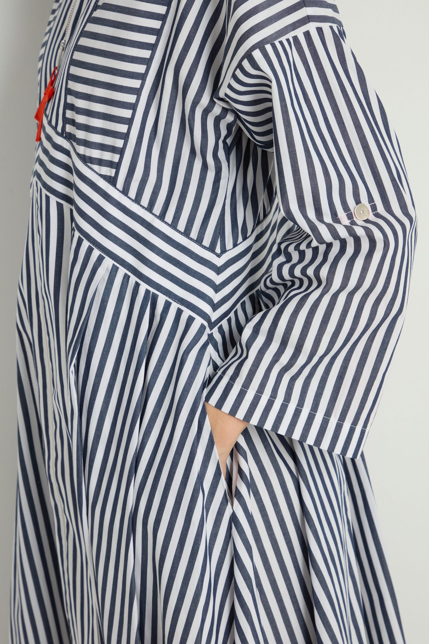 A person wearing the Striped Zip Dress, featuring blue and white vertical and diagonal stripes, stands with one hand in a side pocket.