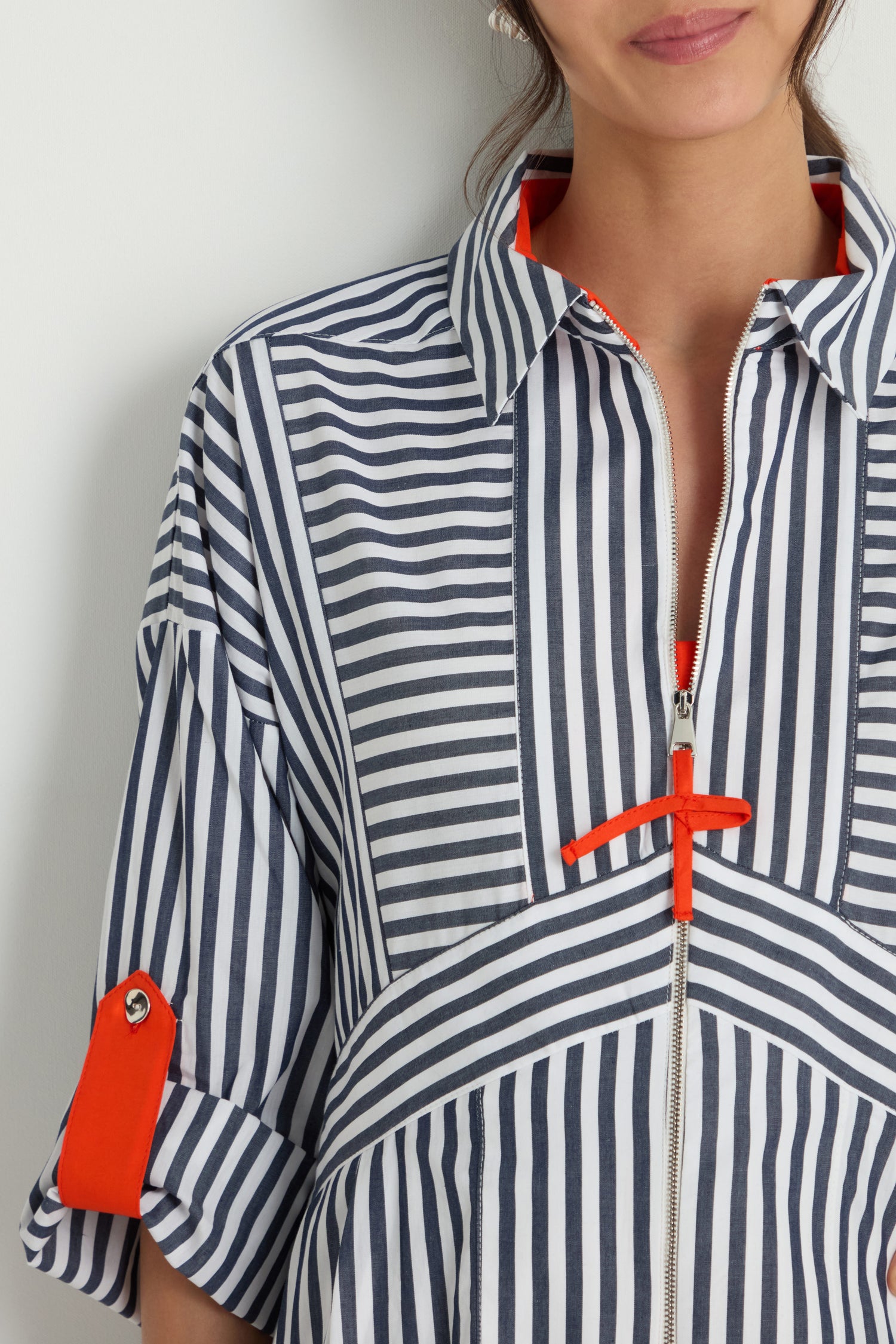 A woman wearing the Striped Zip Dress, featuring navy and white vertical stripes, orange accents, rolled-up sleeves, and a stylish collared neckline.