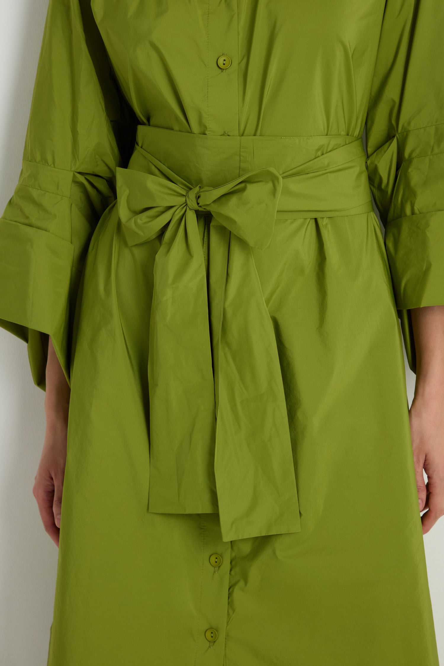 A close-up of the Taffeta Button-Through Lime Dress, a green midi-length piece featuring a large waist bow and elegant front button details.