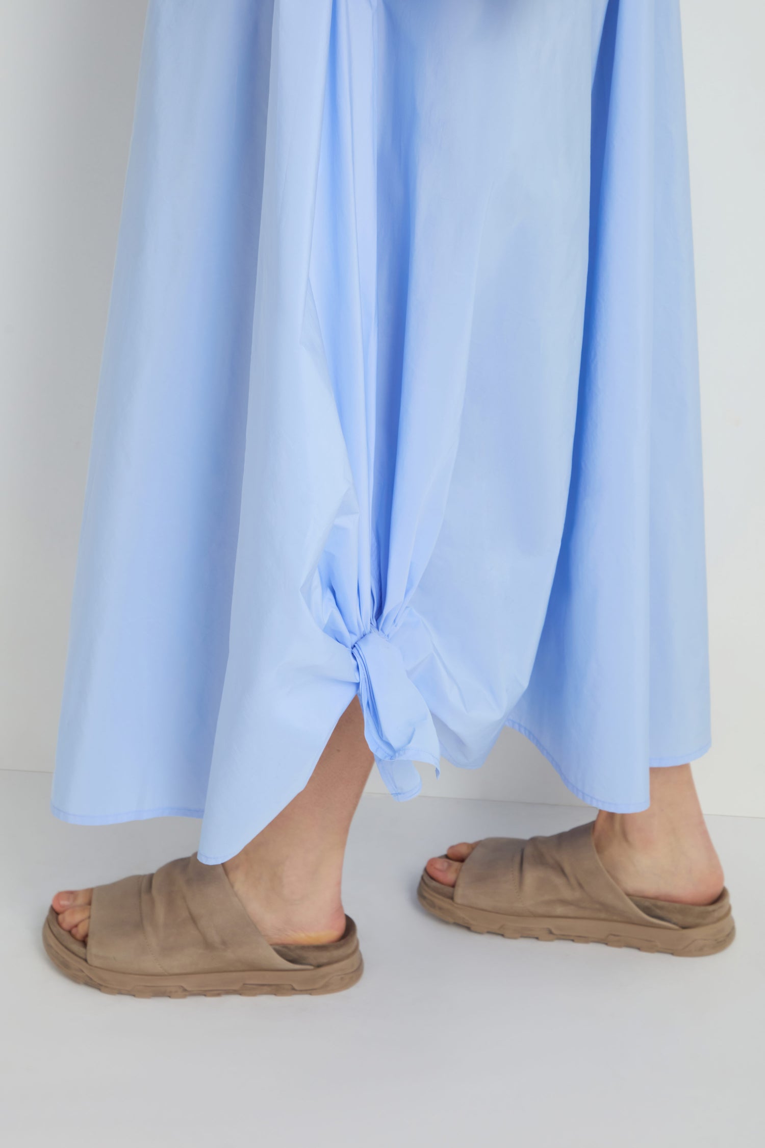 Person wearing the Taffeta Button-Through Sky Dress and beige slide sandals, standing on a white surface.