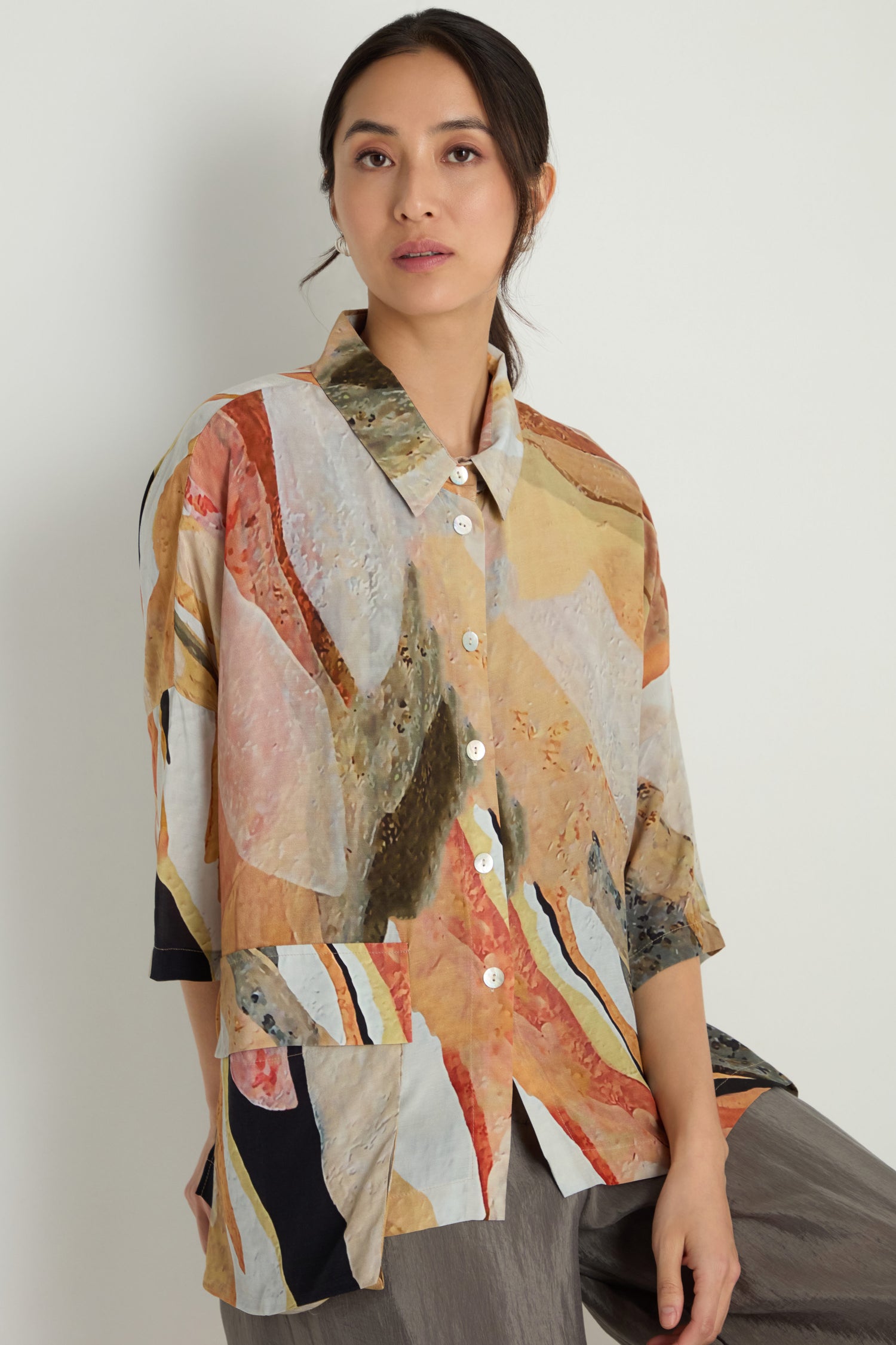 A woman models the Abstract Earth Print Shirt, featuring a relaxed silhouette and soft viscose blend, standing against a plain light-colored wall.