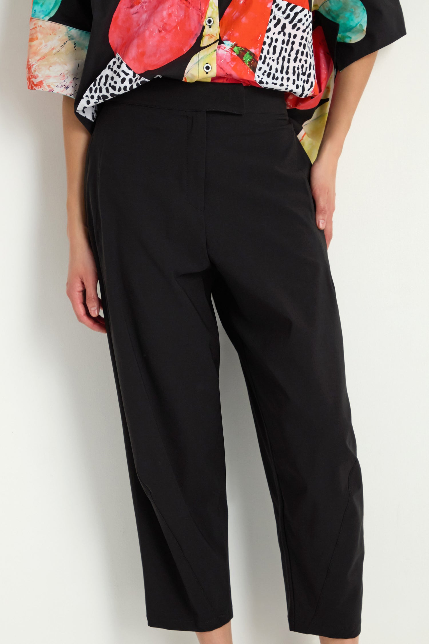 Model wears Slim Leg Trousers in ankle-grazing black with a colorful patterned top, standing against a plain background, hand in pocket.