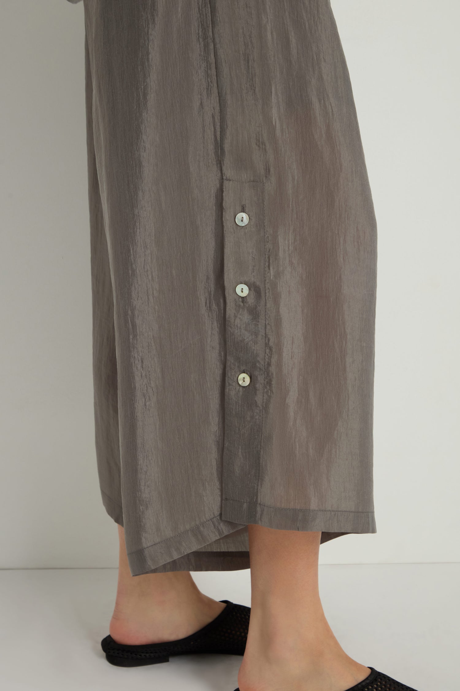 Close-up of a person wearing gray Wide Leg Button Trousers with three white side buttons, standing against a plain background.